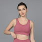 A woman in a Peony Pink Sports Bra and matching leggings stands against a gray background, holding the waistband of her moisture-wicking leggings.