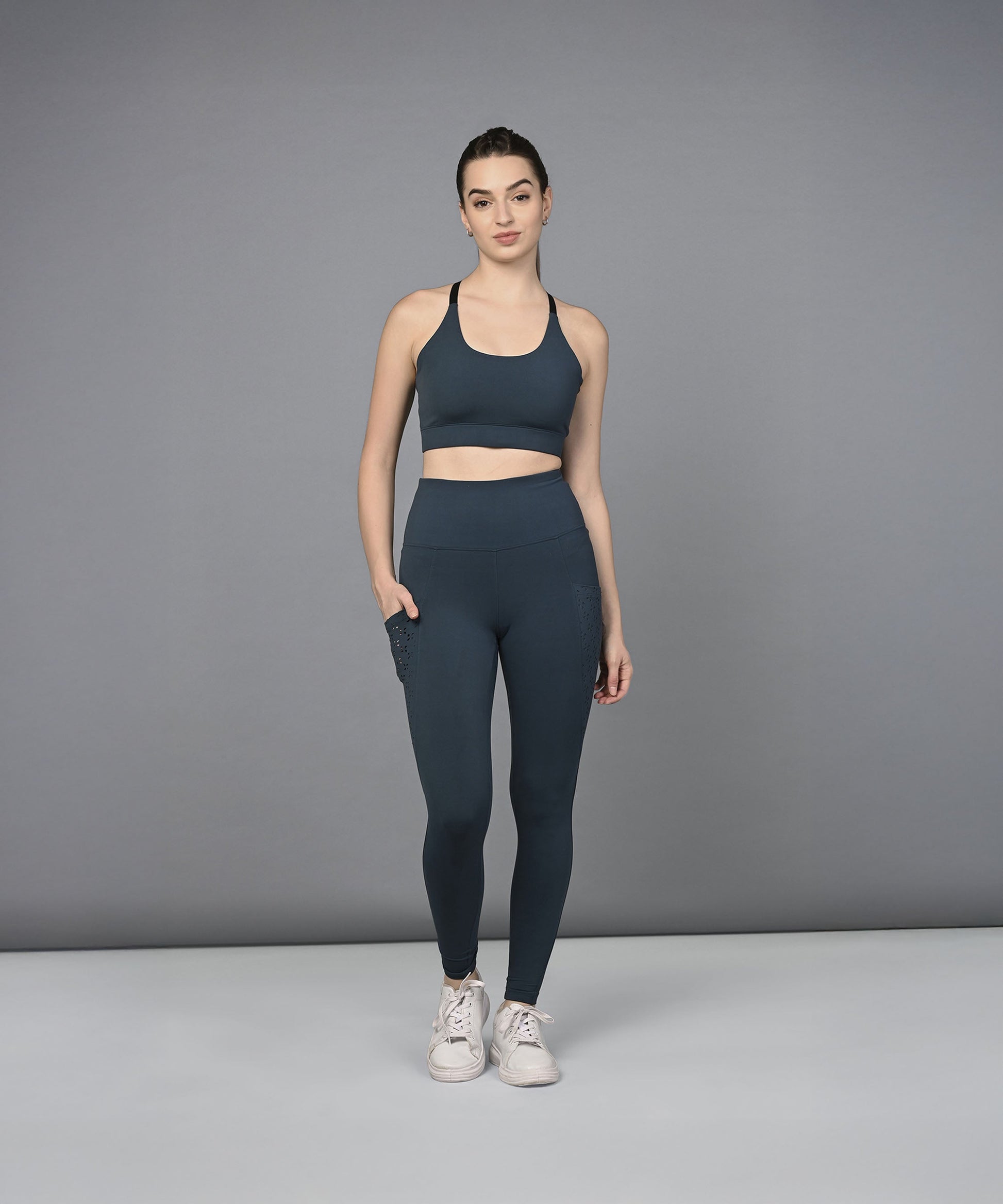 A woman models the Teal Netted Top with blue leggings, standing with one hand in her pocket against a gray background.