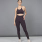 A woman stands confidently in front of a plain gray background wearing the Wine Netted Top paired with a honeycomb self-pattern sports bra and leggings.