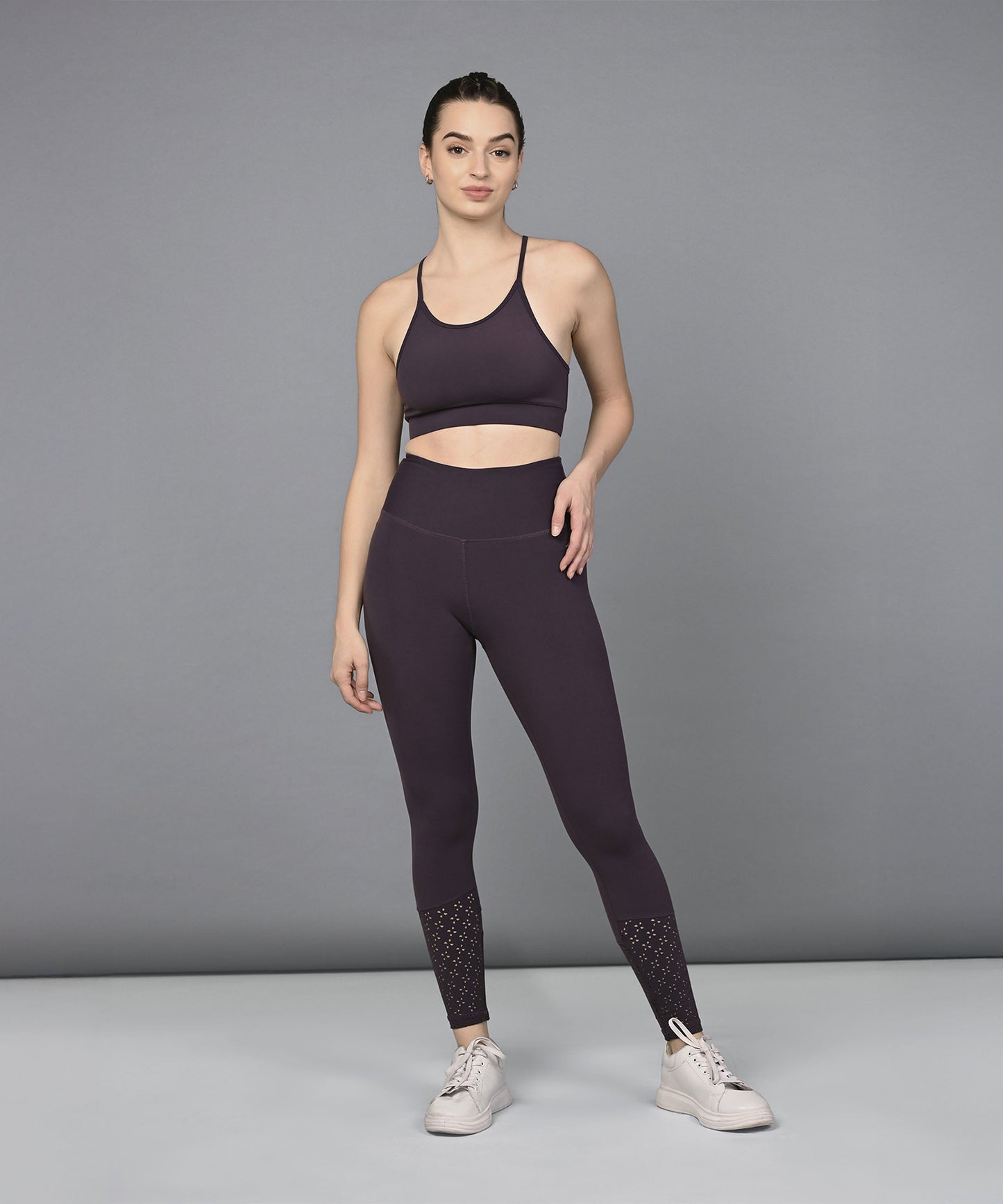 A woman stands confidently in front of a plain gray background wearing the Wine Netted Top paired with a honeycomb self-pattern sports bra and leggings.