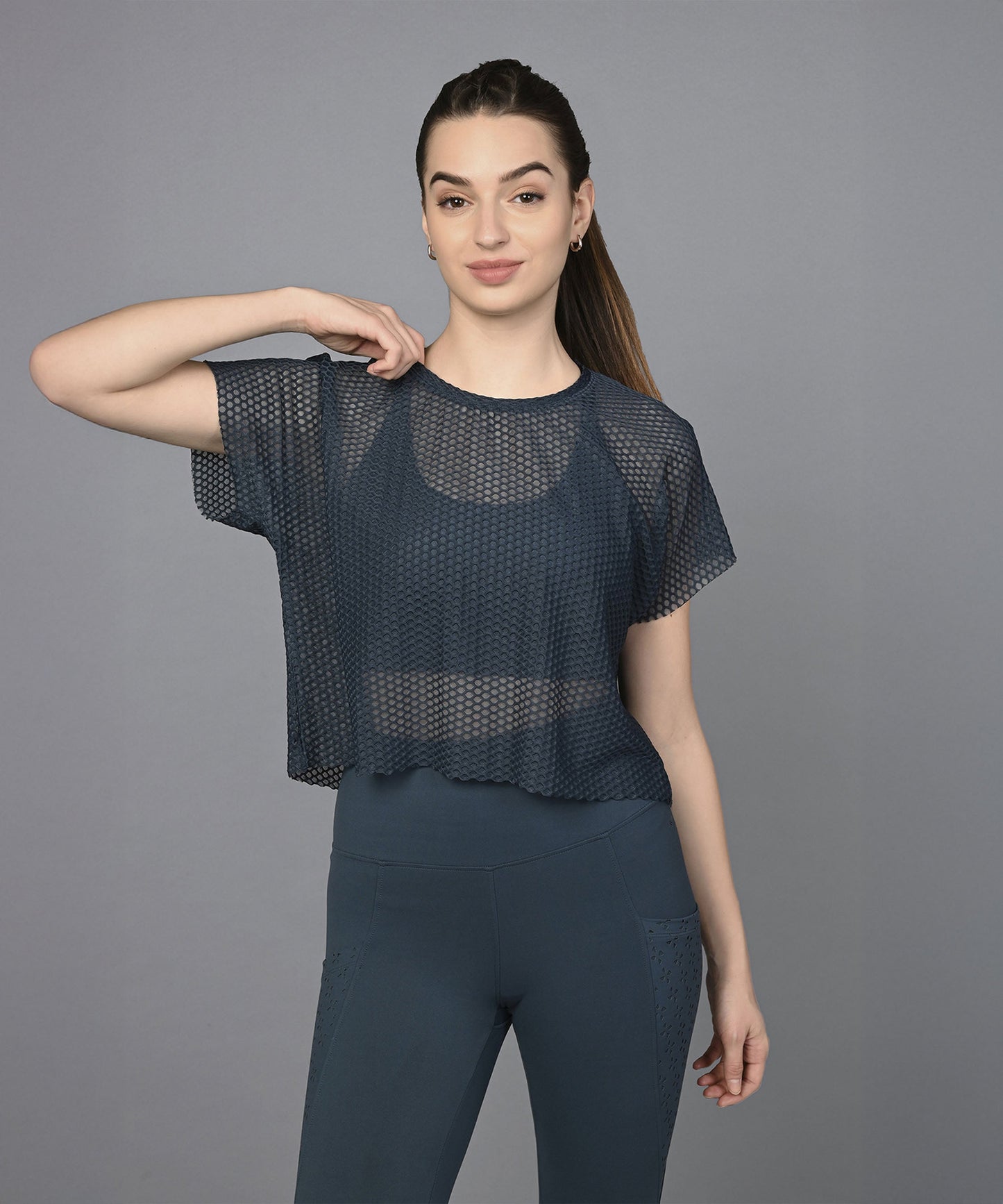 Woman in a Teal Netted Top and matching leggings poses in front of a plain gray background.