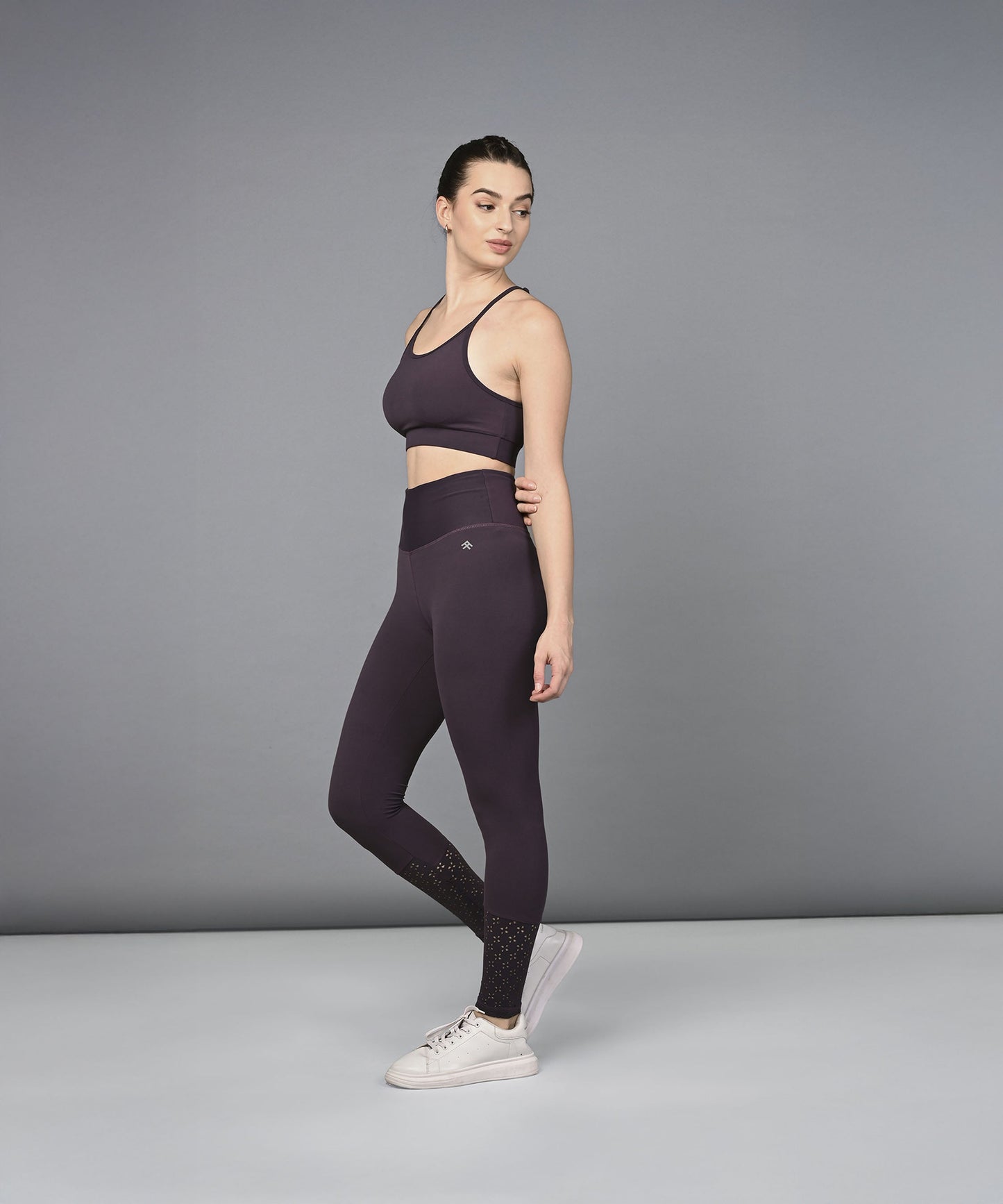 A woman poses sideways against a plain gray background, wearing the Wine Netted Top with matching honeycomb-patterned leggings.
