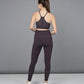 A woman stands with her back to the camera against a gray background, wearing the Wine Netted Top in dark purple athletic wear with a honeycomb self pattern and white sneakers.