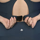 Close-up of hands fastening the back of a teal, moisture-wicking Teal Sports Bra, with a small logo visible on the leggings below.