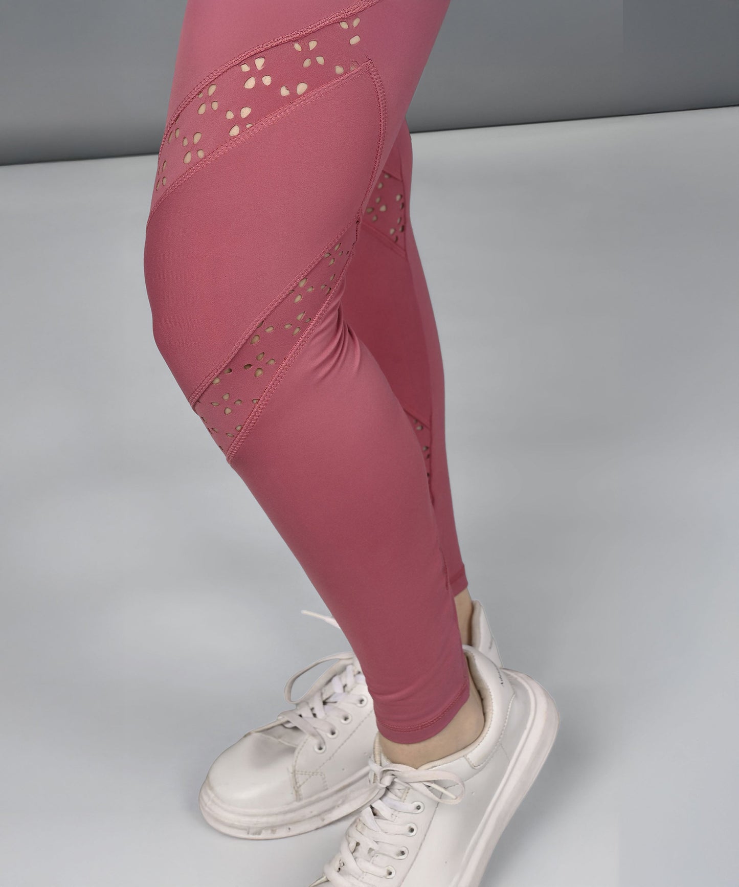 Person wearing Peony Pink Leggings with mesh cutouts and white sneakers, standing on a light gray surface.