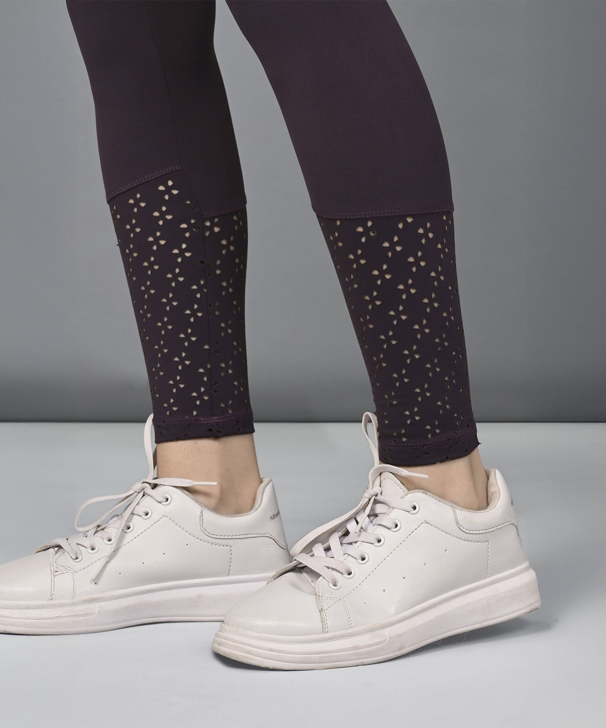 A person wearing white sneakers and black leggings with a cutout pattern near the ankles, paired with the Wine Netted Top.