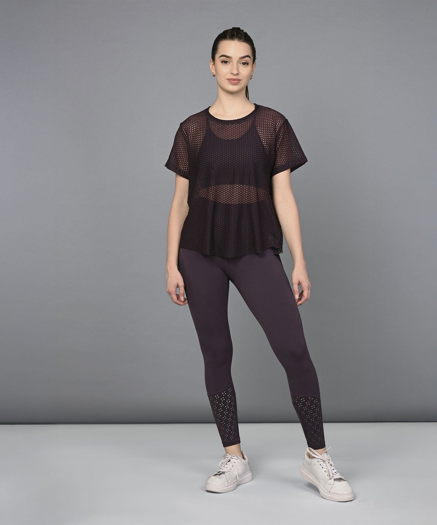 Woman wearing a Wine Netted Top and matching mesh leggings, styled with white sneakers, standing against a plain grey background.