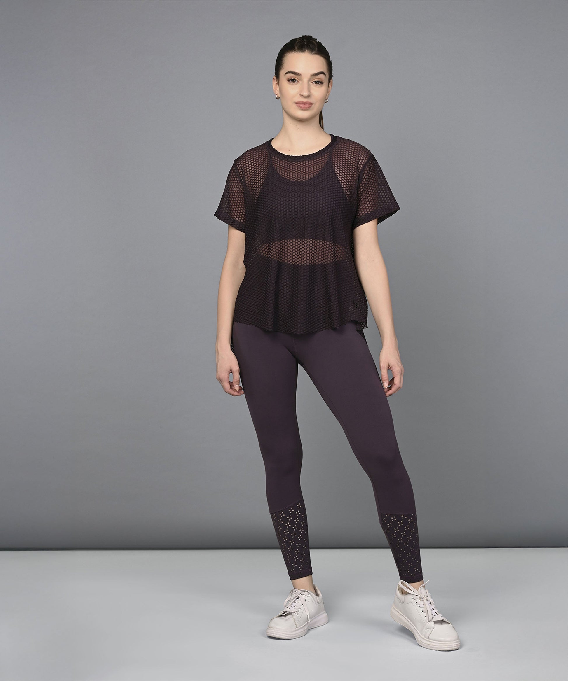 Woman wearing a Wine Netted Top and matching mesh leggings, styled with white sneakers, standing against a plain grey background.