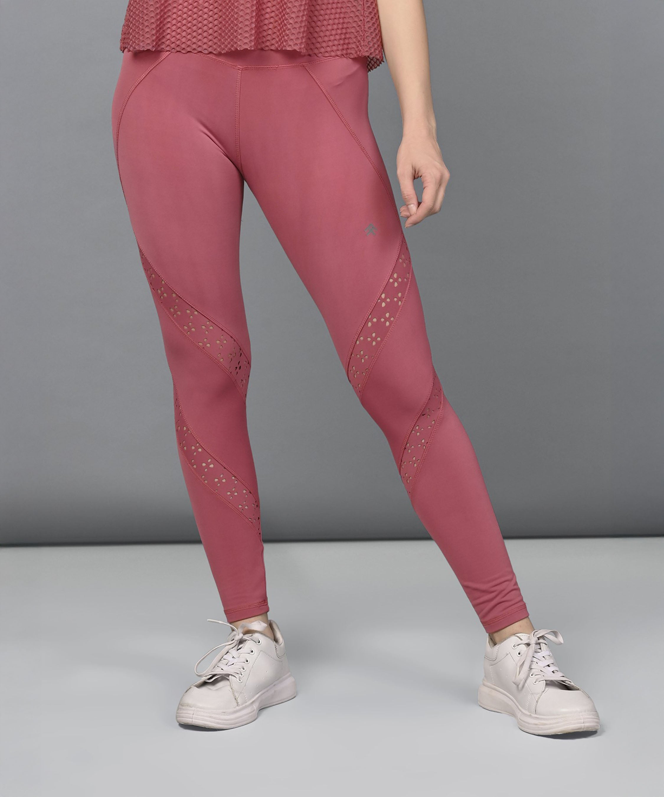 Model showcases Peony Pink Leggings featuring mesh panels, paired with white sneakers, standing against a plain gray background.