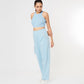 Woman wearing the Blossom Blue Set with a light blue sleeveless crop top and cargo track pants, standing and looking down against a white background.