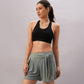 A woman wearing the Black Sports Bra with adjustable straps and green shorts stands against a plain background, looking to the side.