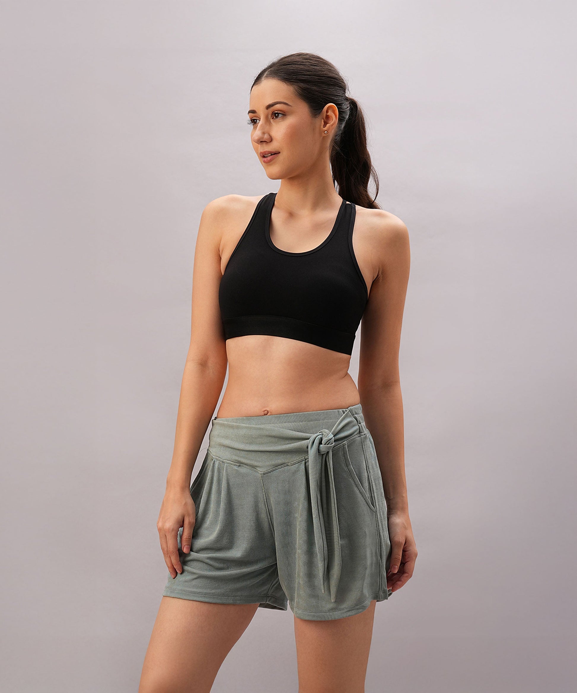 A woman wearing the Black Sports Bra with adjustable straps and green shorts stands against a plain background, looking to the side.