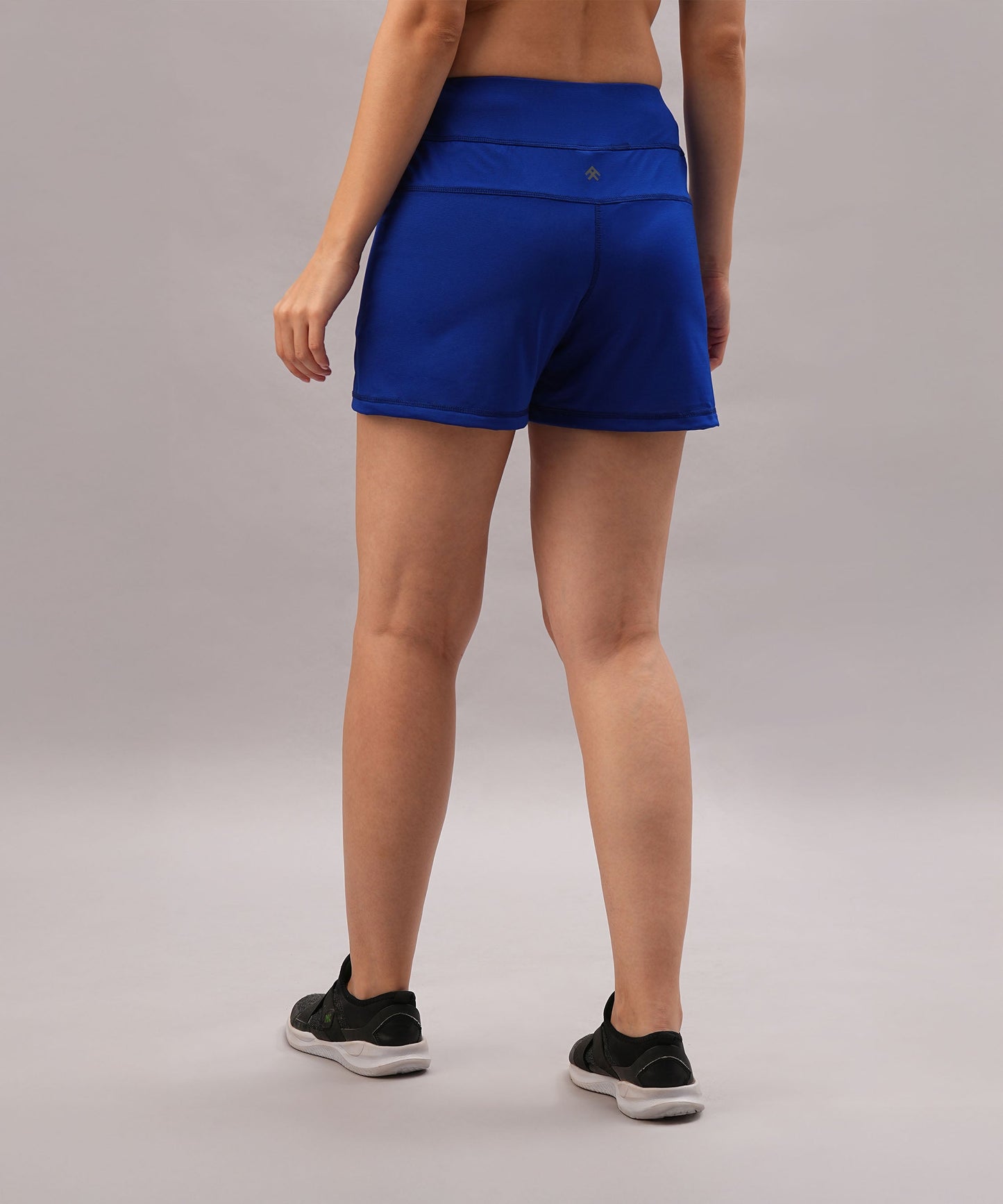 Person wearing Blue Premium Stretch Shorts With Lining and black shoes stands on a gray background, facing away from the camera.