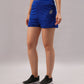 A woman stands against a plain light background wearing Blue Premium Stretch Shorts With Lining, paired with black slip-on sneakers.