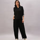 Woman in a Black Rayon Co-Ord Set featuring a chic top and relaxed pants, paired with white sneakers, stands with one hand in her pocket against a plain background.