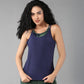 Woman with long curly hair wearing a Tie & Dye Bra T shirt over a green top, standing against a gray background.
