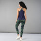 A woman faces away on a plain grey background, wearing the Tie & Dye Bra T shirt in green over a navy tank top.
