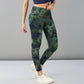 A woman models Tie & Dye Leggings in green stretchy fabric, paired with white sneakers and a blue top, standing against a plain gray background—ideal for enhancing your workout wardrobe.