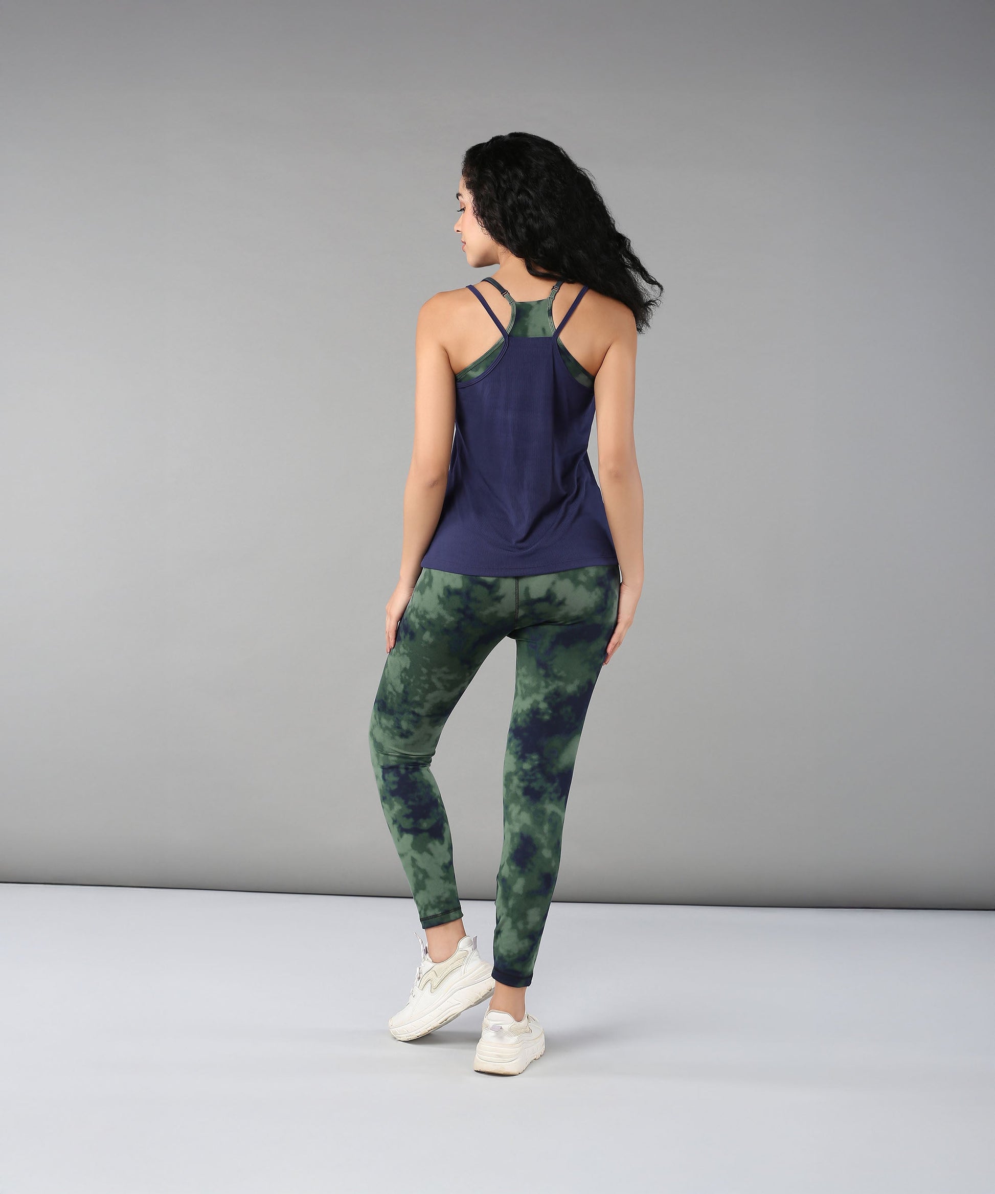 A woman stands with her back to the camera in a navy tank top and Tie & Dye Leggings, highlighting a stylish workout wardrobe crafted from stretchy fabric.