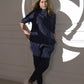 A woman in the Accented Set, a navy cotton co-ord, stands against a white wall with circular shadow patterns, hands in pockets.