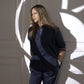 A woman in the Accented Set, a chic cotton co-ord, stands against a white wall with elegant abstract shadows behind her.
