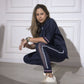 A woman wearing the Accented Set, a navy cotton co-ord, squats indoors against a white paneled wall, looking at the camera.