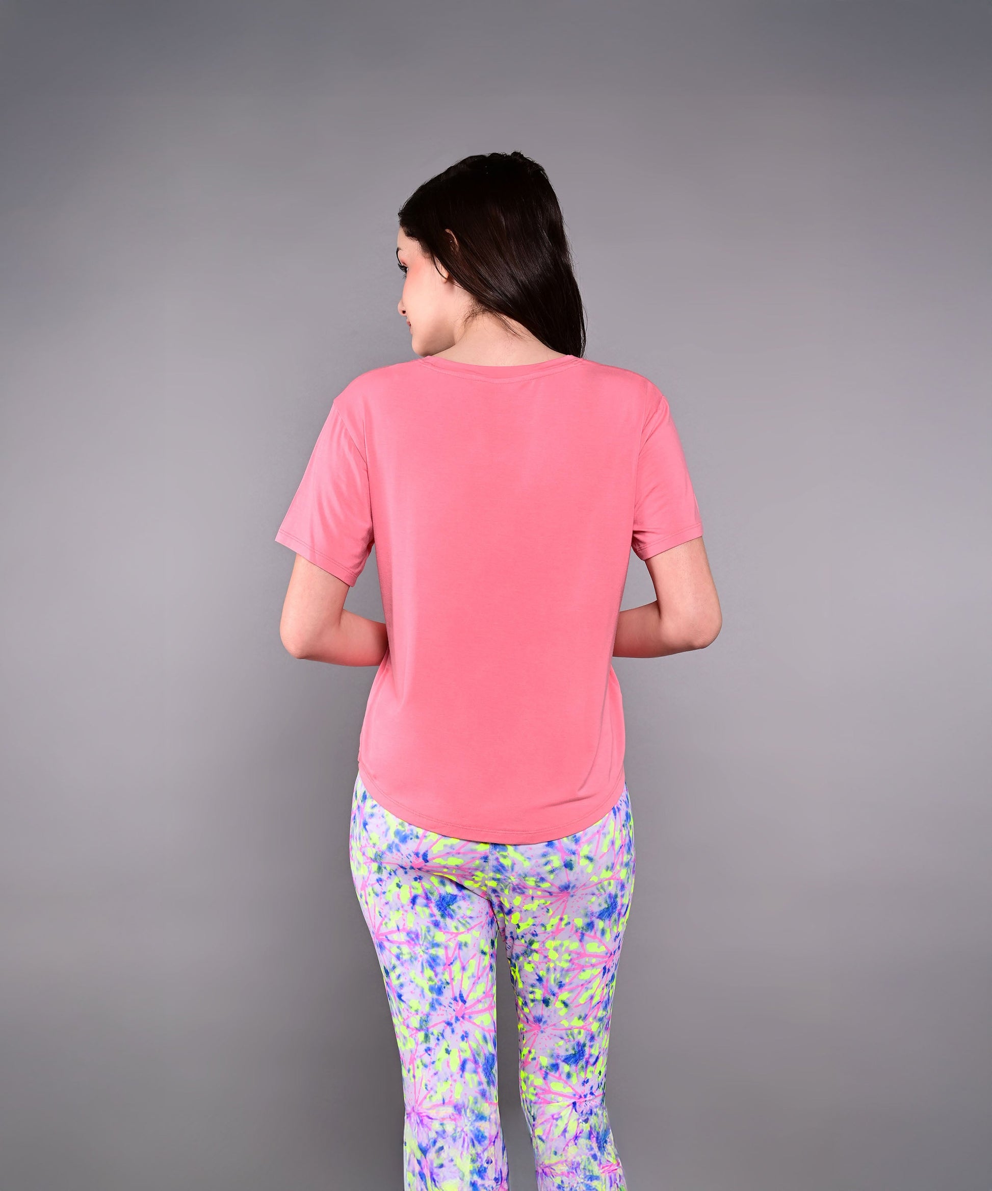 Back view of a woman wearing a pink Adore Your Core printed tee paired with colorful leggings