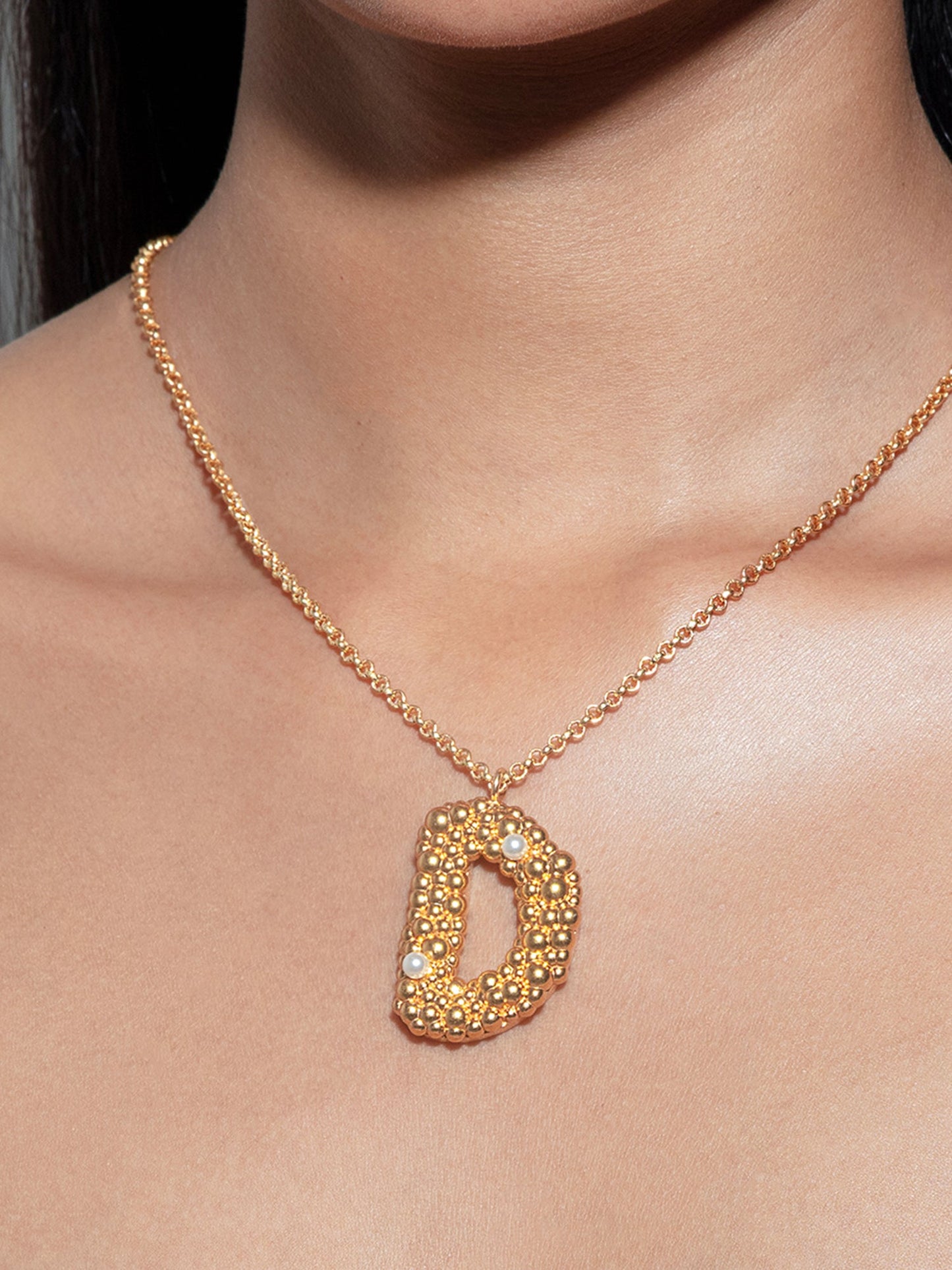 Stylera gold letter D necklace with textured floral pendant and chain worn on model neckline