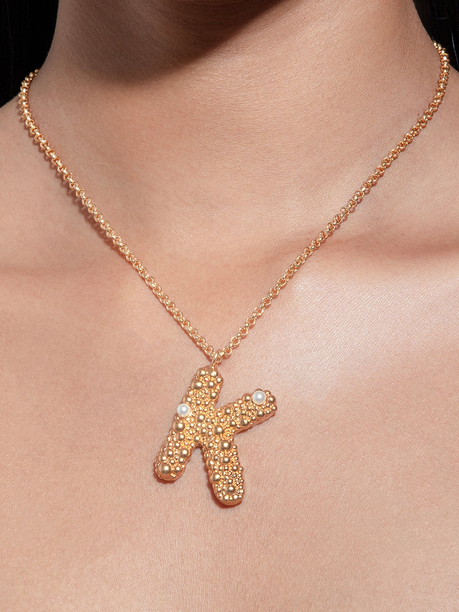 Stylera textured pendant worn on model featuring gold letter K necklace with pearl accents on delicate chain