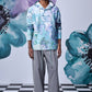 Male model wearing artistic print hoodie shirt by Stylera in pastel blue floral print with gray wide leg trousers