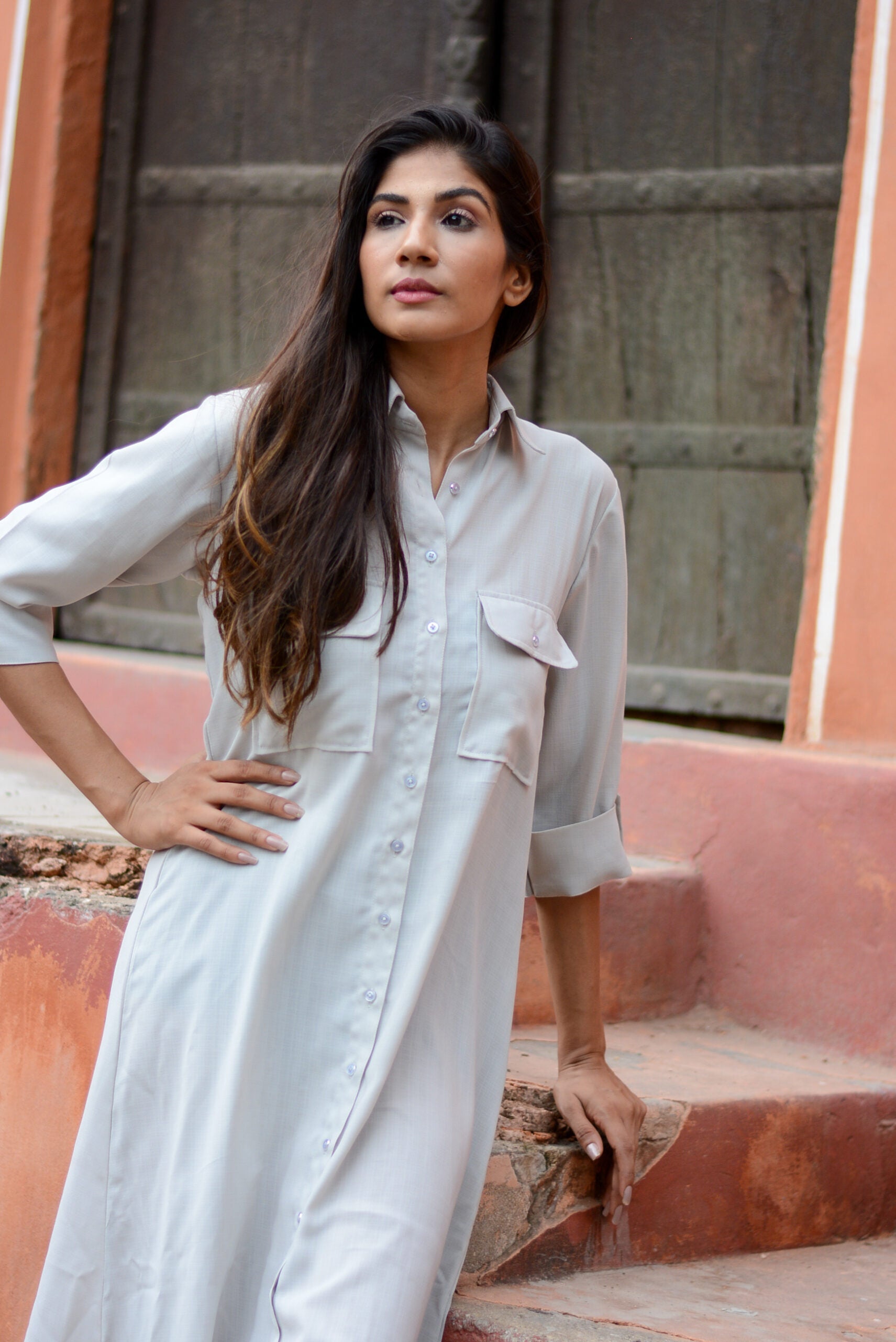 Model wearing an ash grey midi shirt dress with button details and a chest pocket in a rustic setting