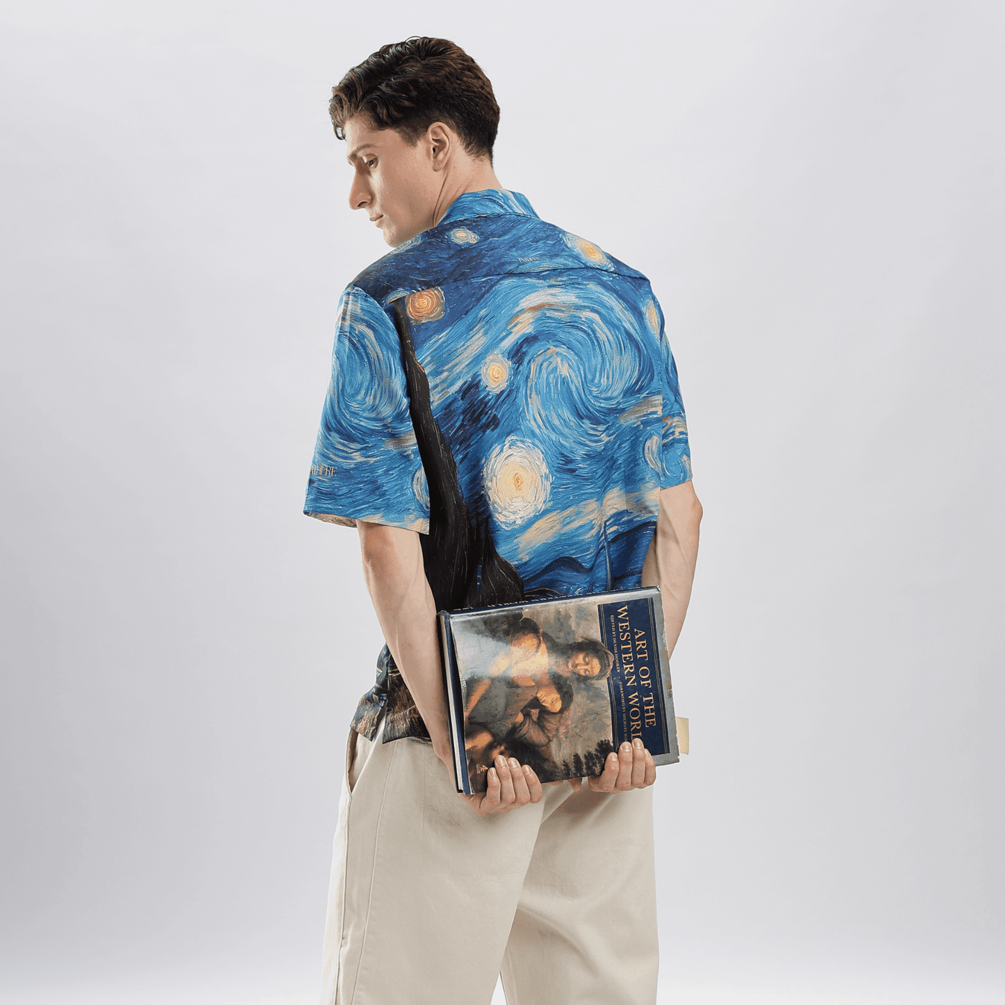 Back view of model wearing Stylera men's art print casual shirt with Starry Night design holding an art book