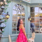 Woman in pink Barbie balloon dress posing by teal cafe with floral decor vintage chairs and arched windows