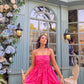 Woman modeling Stylera Barbie balloon dress in bright pink short fit and flare with thin straps by floral cafe backdrop