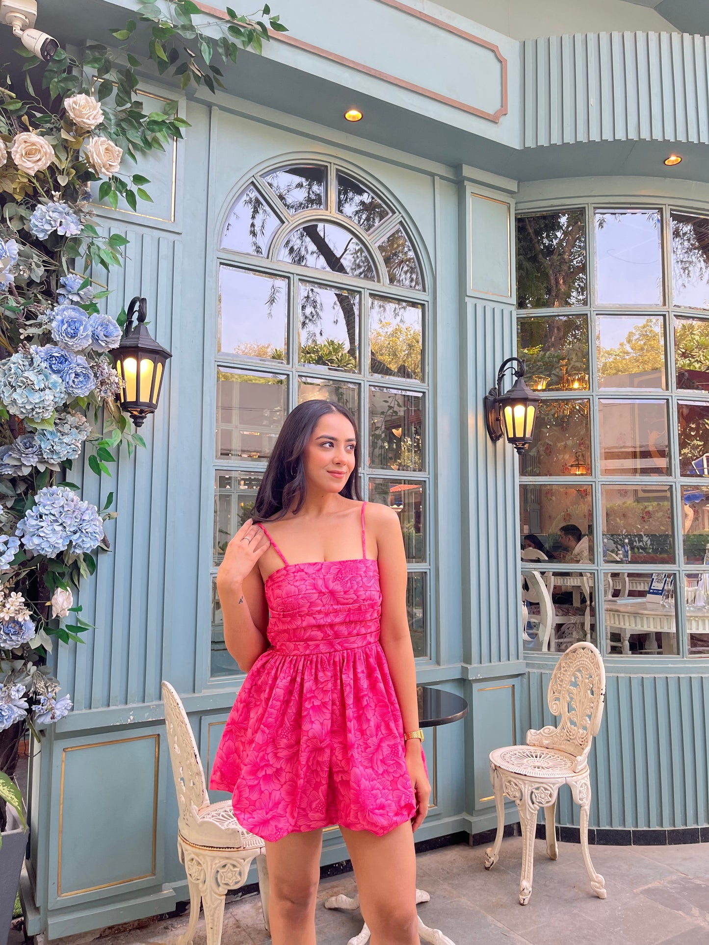 Woman in a hot pink Barbie balloon dress standing outside a mint cafe with floral decor