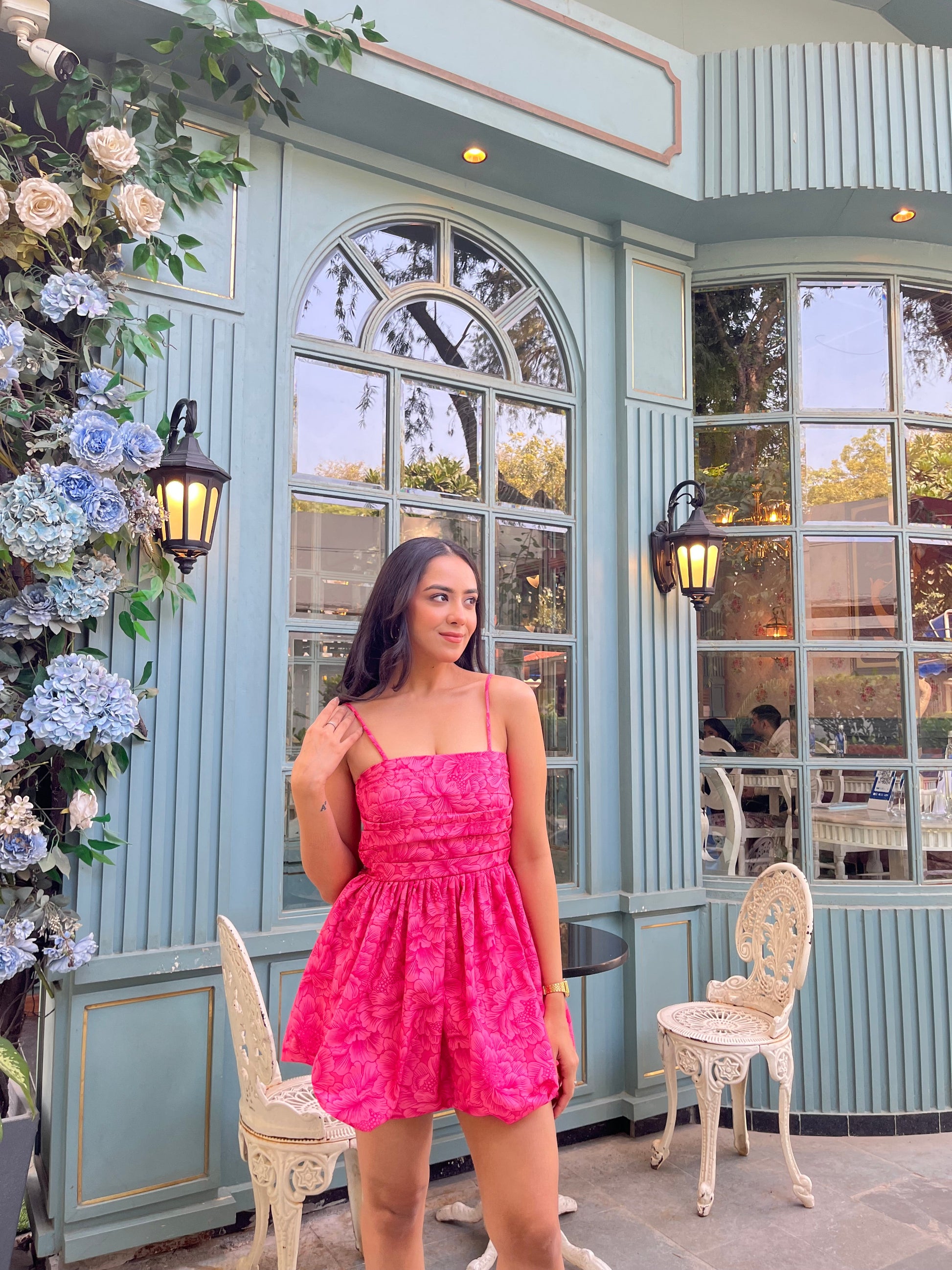 Woman in a hot pink Barbie balloon dress standing outside a mint cafe with floral decor