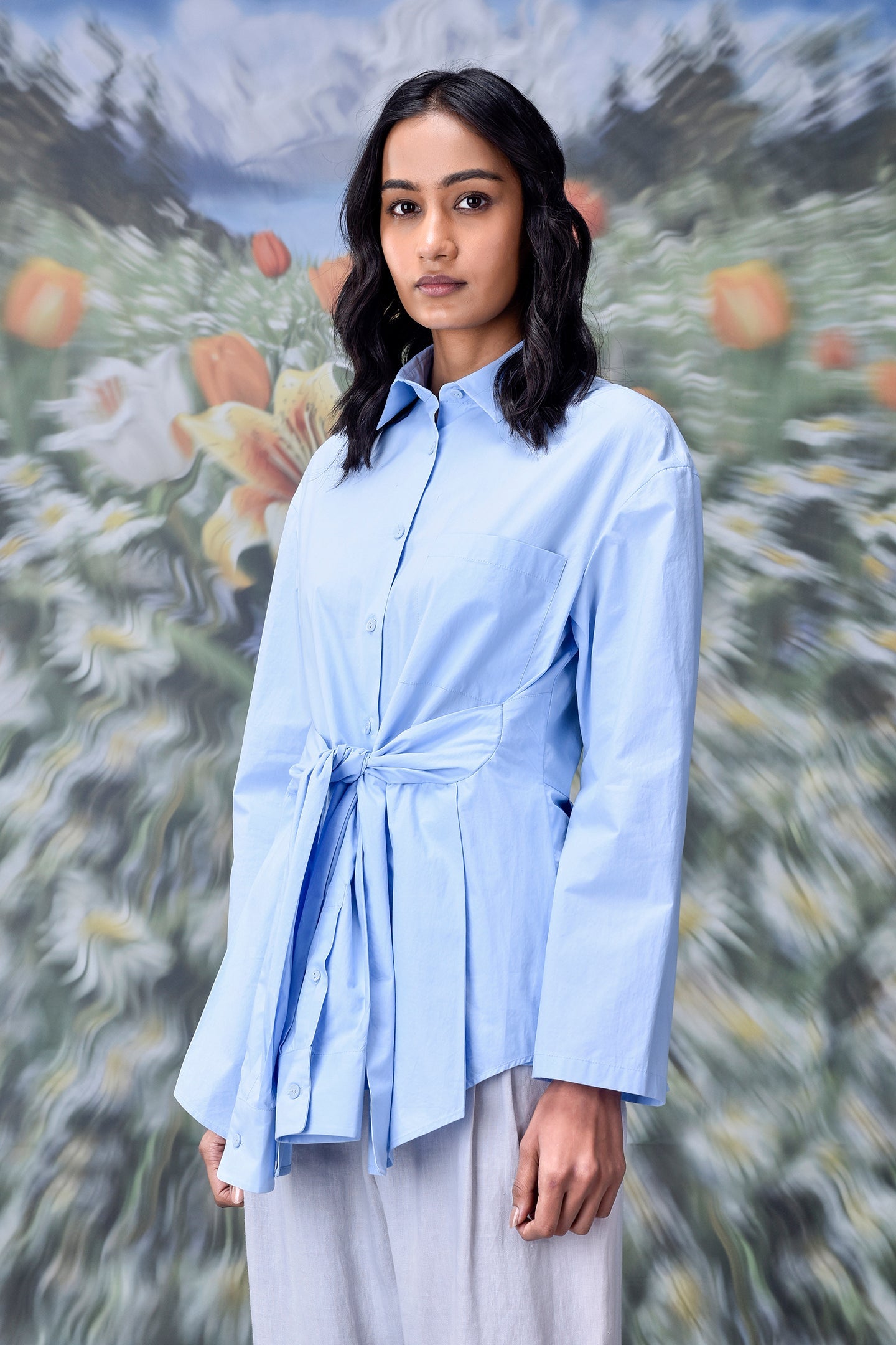 Stylera model wearing unique casual light blue shirt for women with tie front waist and long sleeves