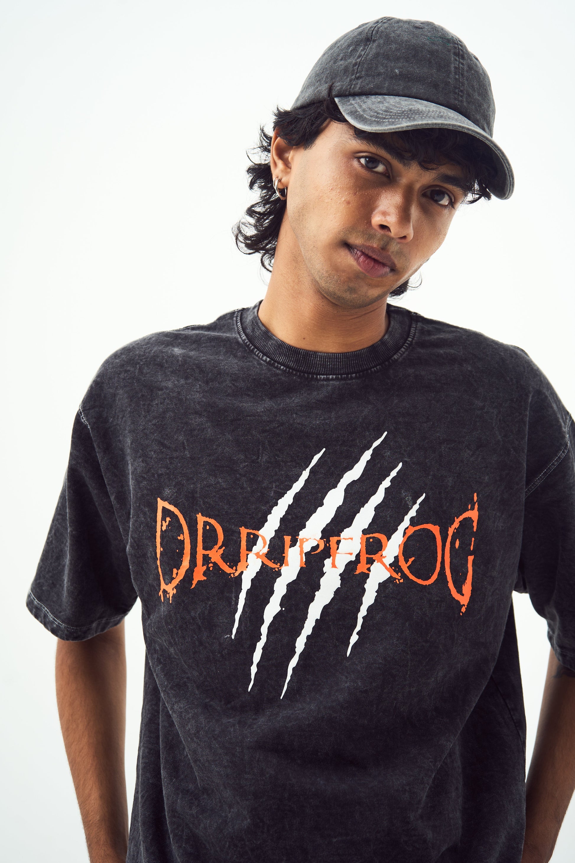 black acid wash oversized t-shirt Stylera logo with white claw marks and orange lettering modeled by young man wearing black cap