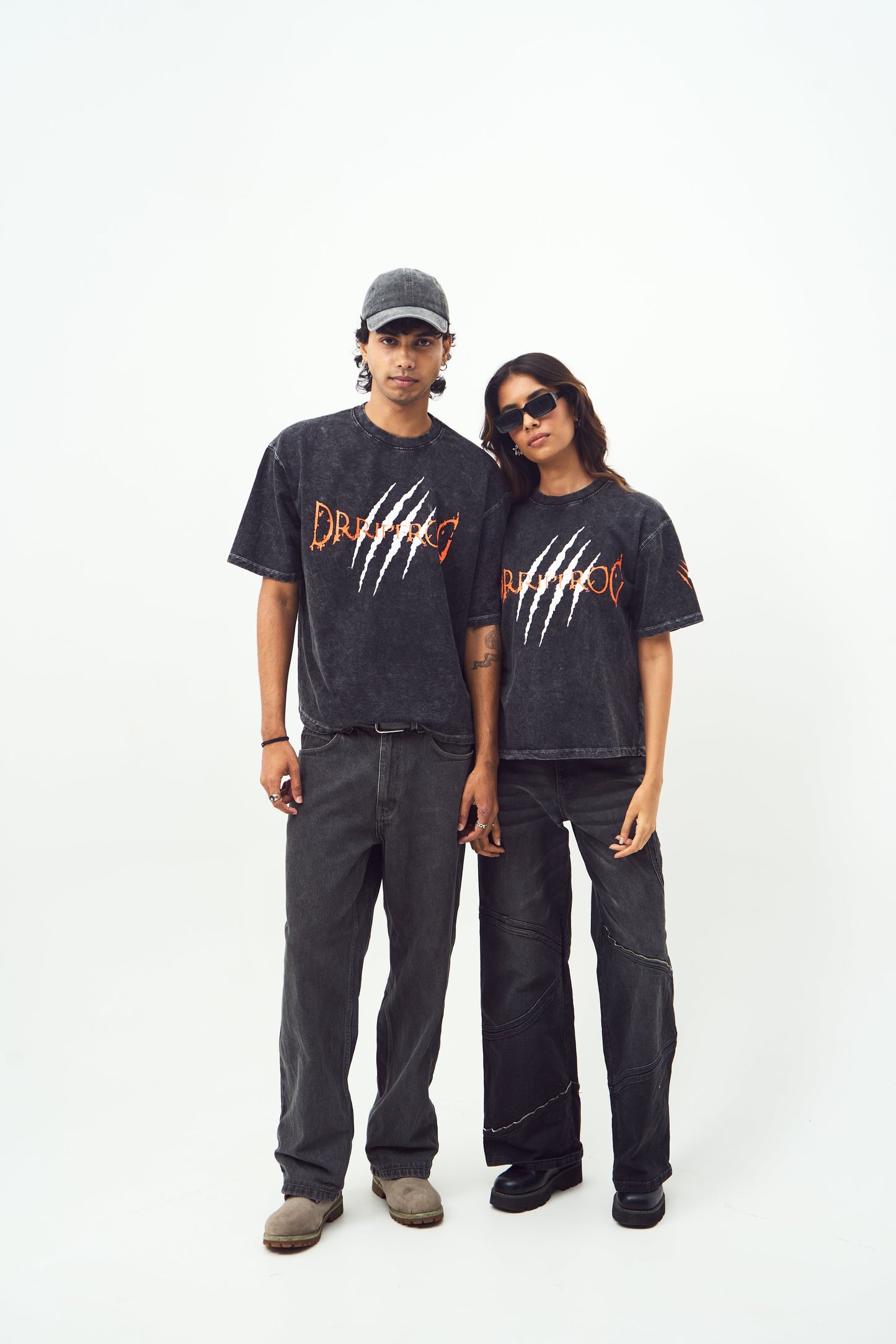 Male and female models wearing Stylera black acid wash oversized t-shirt with claw graphic paired with black pants