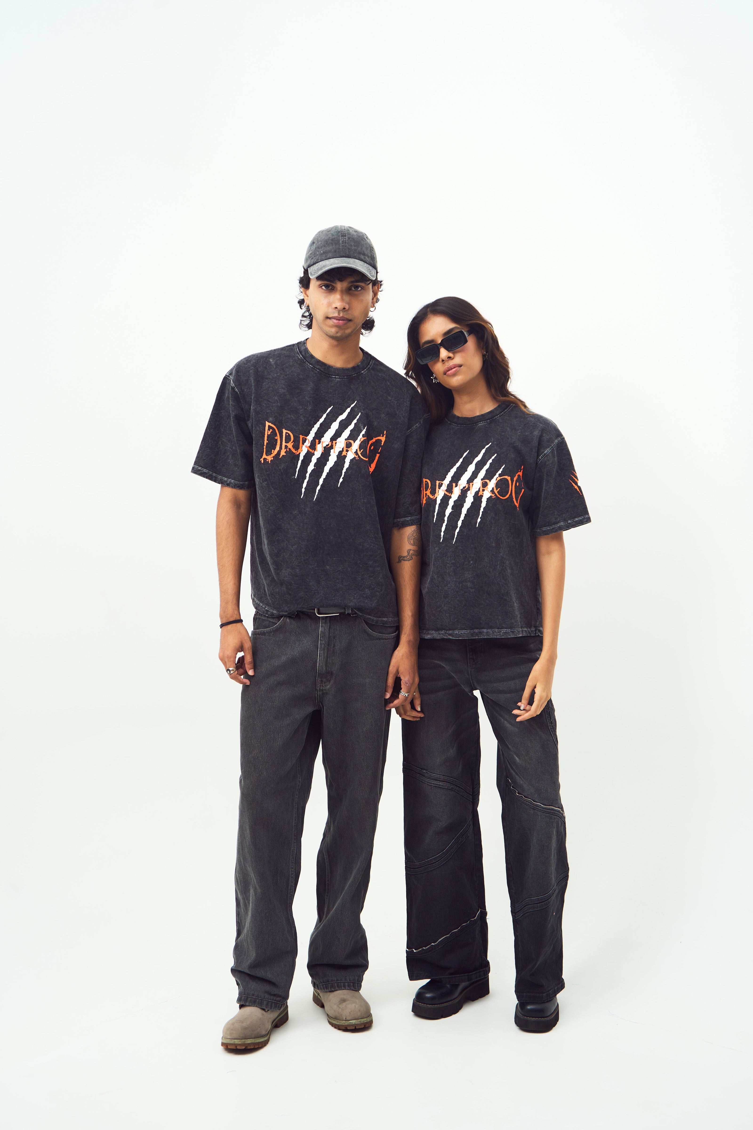 Male and female models wearing Stylera black acid wash oversized t-shirt with claw graphic paired with black pants