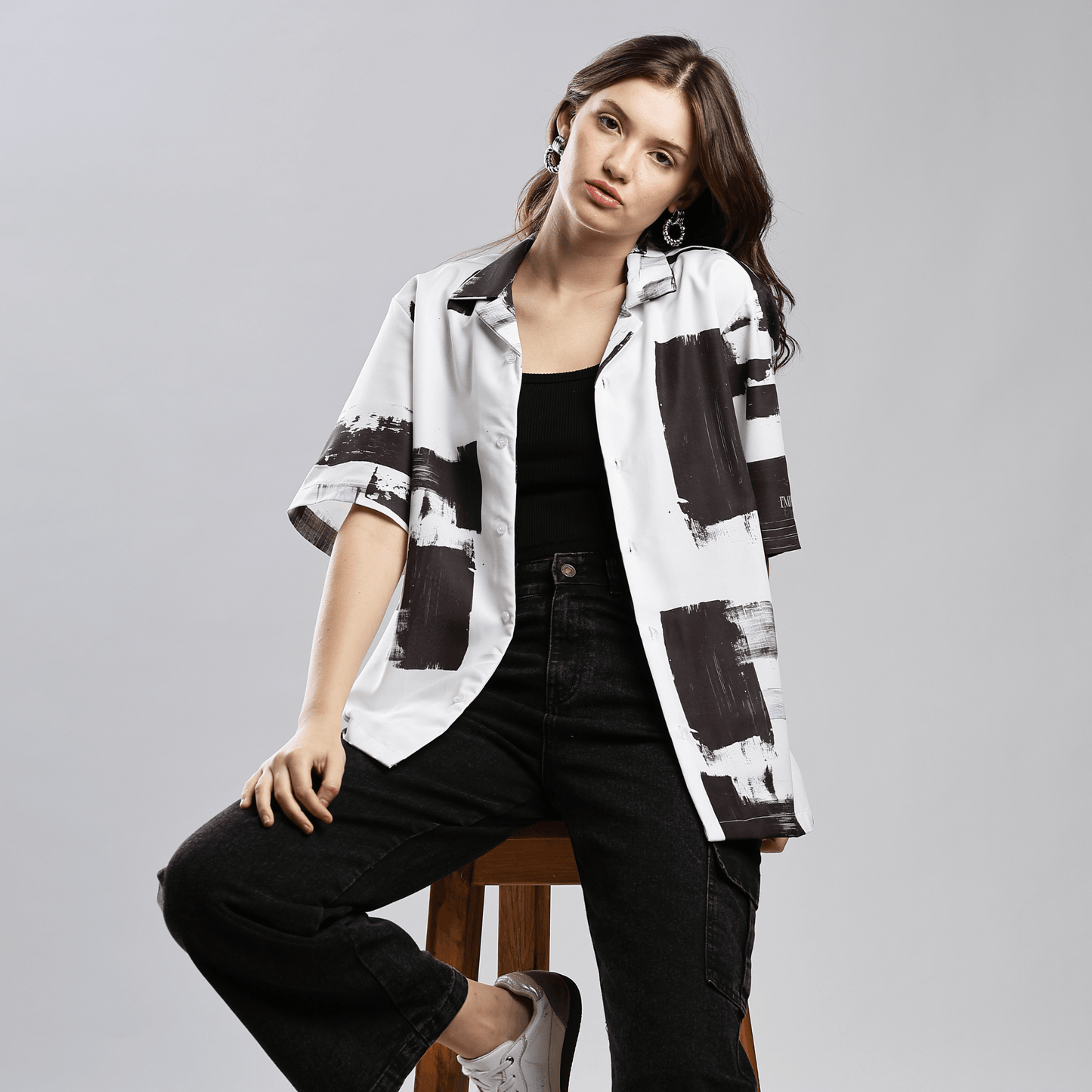 Female model wearing Stylera black and white artsy shirt for men short sleeve button up over black tank and jeans