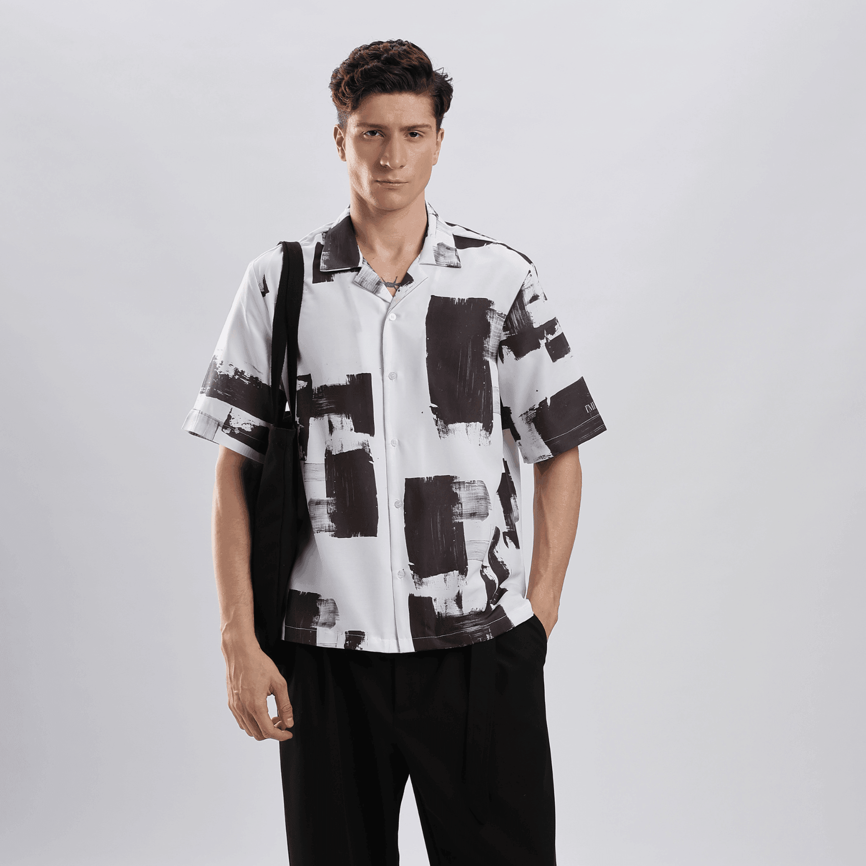 Stylera black and white artsy shirt for men shown on male model wearing short sleeve brushstroke print shirt with black tote