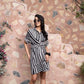 Woman wearing black and white wrap dress by Stylera standing against a textured stone wall