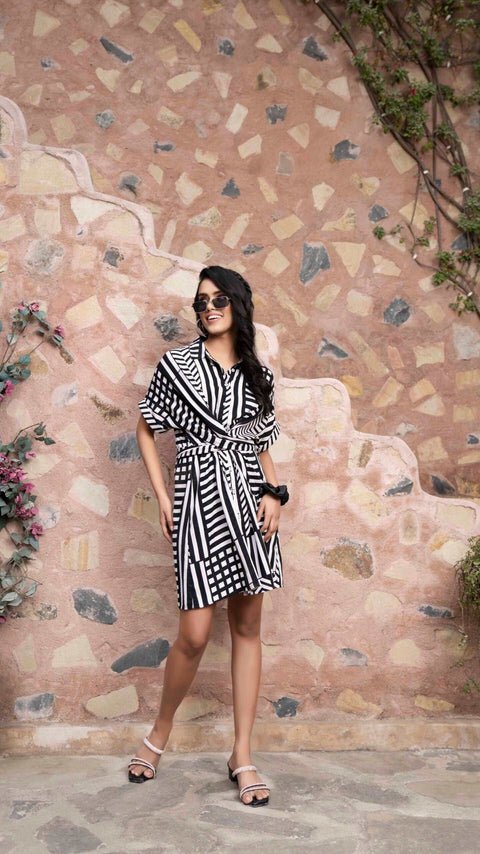 Woman wearing black and white wrap dress by Stylera standing against a textured stone wall