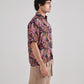 Man wearing a black floral drop shoulder shirt, featuring vibrant tropical patterns and short sleeves