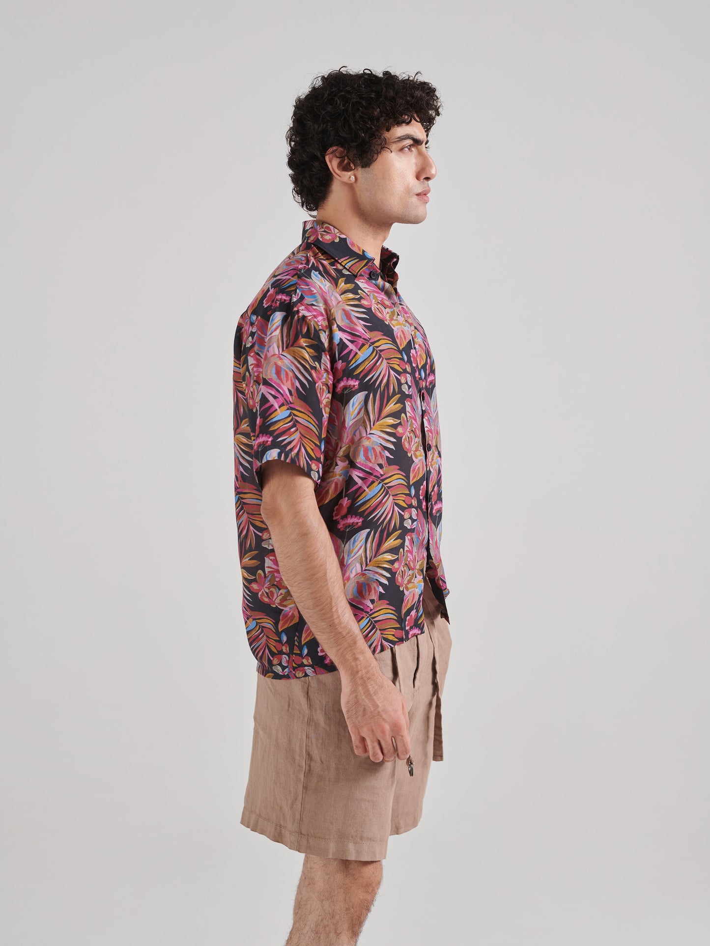 Man wearing a black floral drop shoulder shirt, featuring vibrant tropical patterns and short sleeves