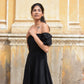 Model wearing a black off shoulder short dress with puff sleeves in a sunny outdoor setting