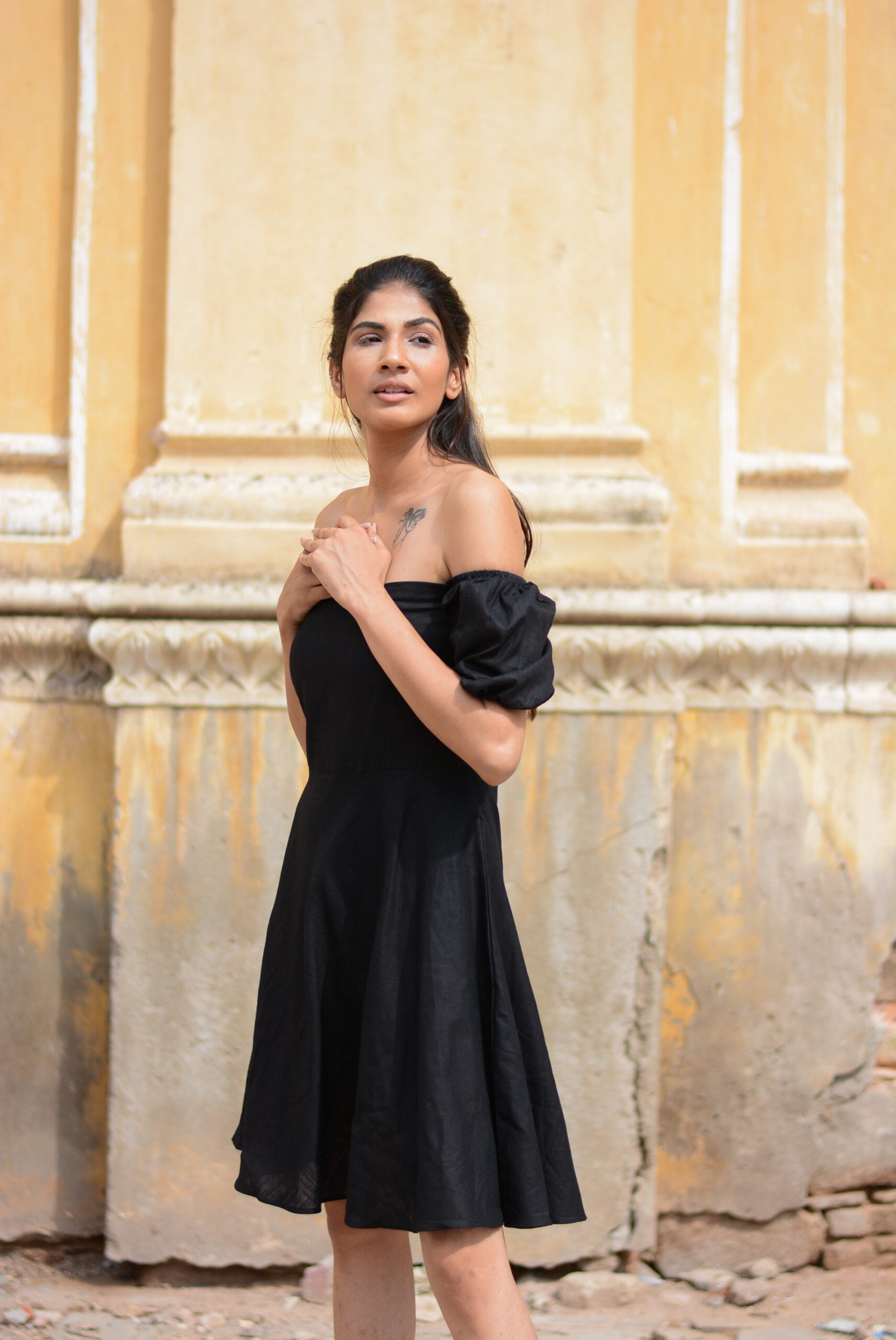 Model wearing a black off shoulder short dress with puff sleeves in a sunny outdoor setting