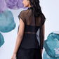 Back view of model wearing black organza top for women layered over bandeau with textured mini skirt