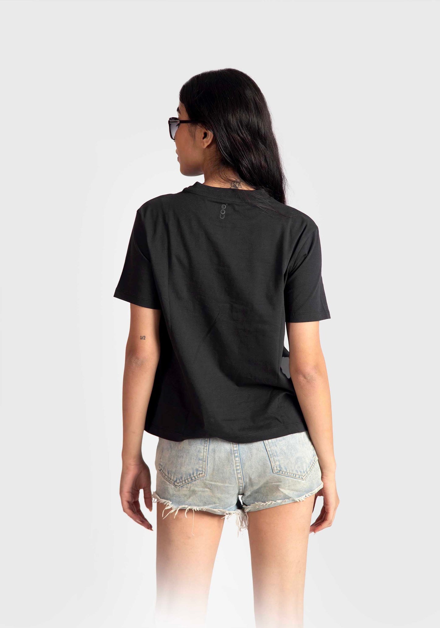 Back view of a woman wearing a black print t-shirt for women paired with denim shorts